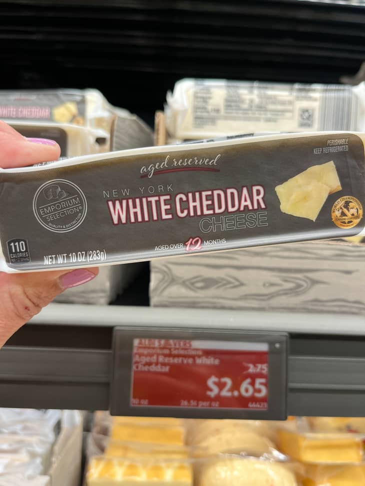 Someone holding block of white cheddar cheese.