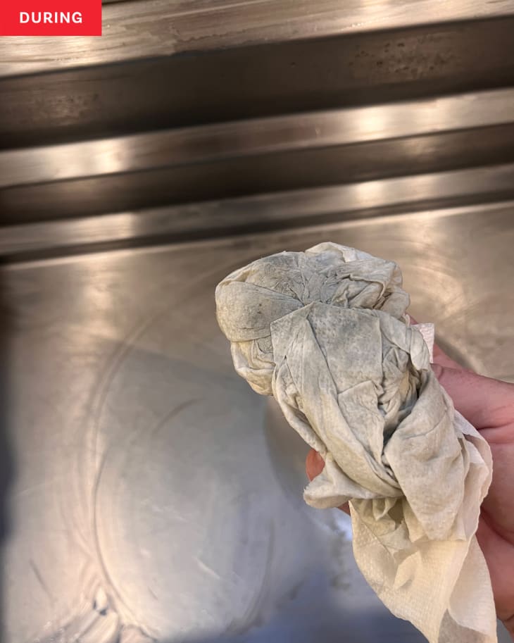Someone holding up cleaning rag after wiping out stainless steel sink.