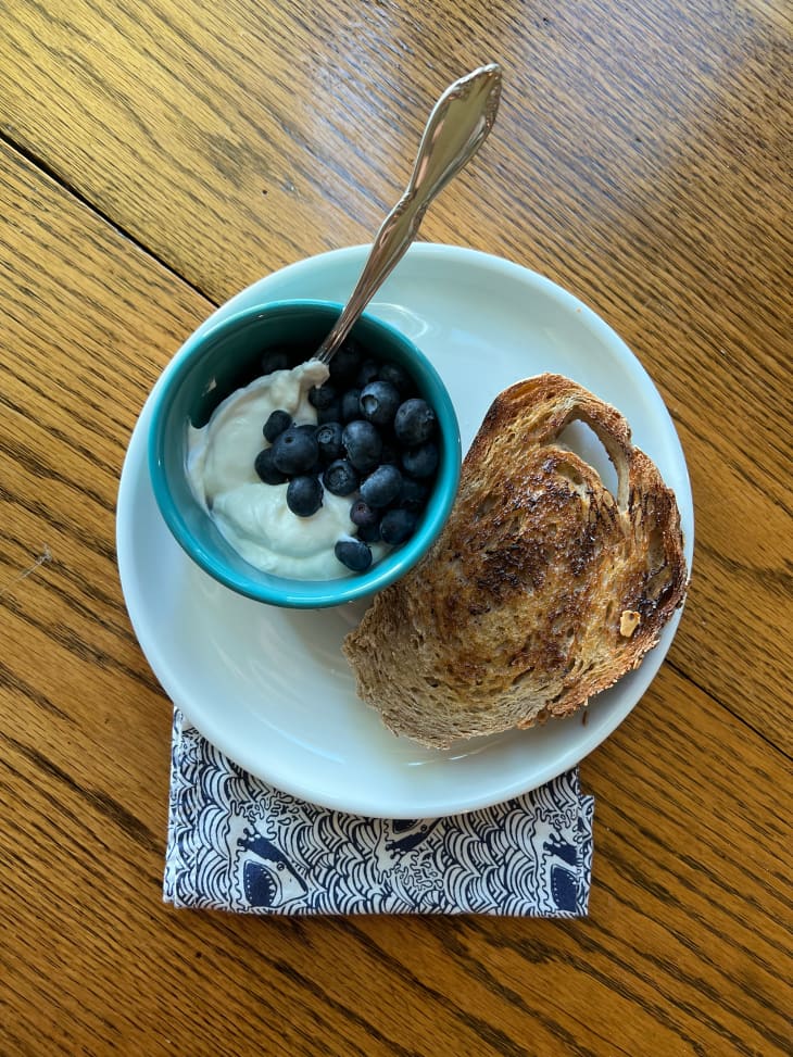 Breakfast of toasted bread and yogurt with blueberries on dining table.