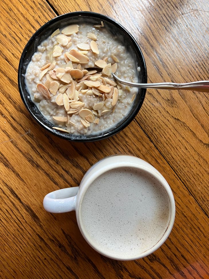 Bowl of oatmeal topped with almonds and mug of latte on the side.