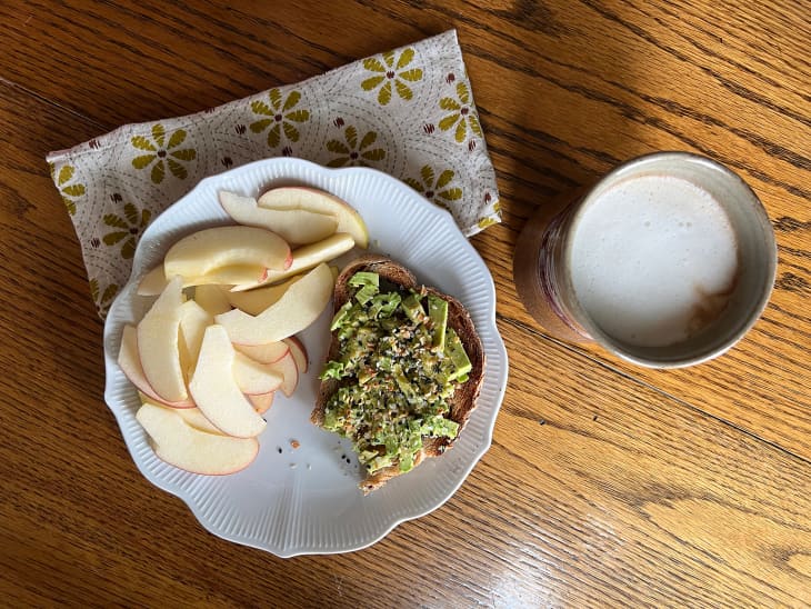 Sliced apples and avocado toast on plate with latte in mug on the side.