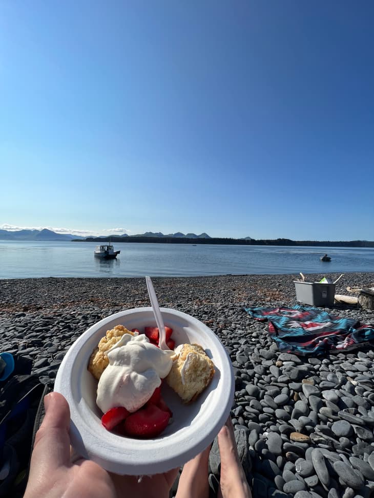 Someone holding bowl of strawberry shortcake while hanging out on a rocky beach.