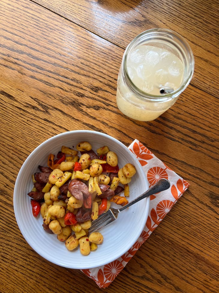 Bowl of pasta with sausage and peppers. Beverage with metal straw on the side.