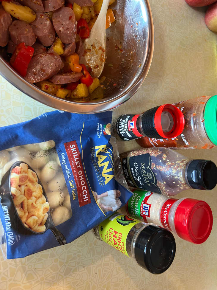 Packaged gnocchi on surface surrounded by spices and bowl of sausages on the side.