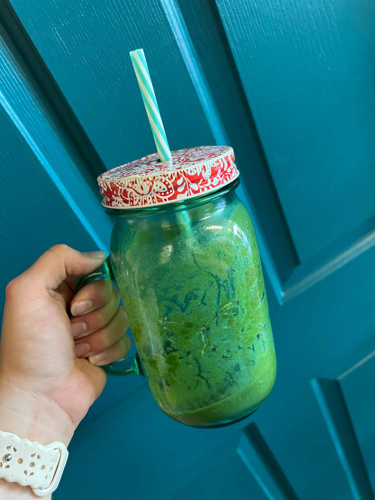 Someone holding glass mug with green smoothie.