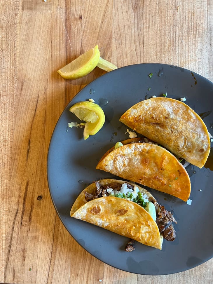 Three hard shelled beef tacos on plate with lemon on the side.