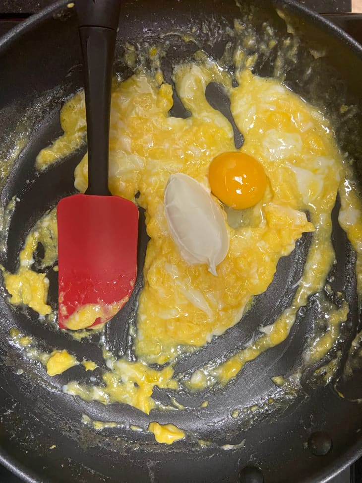 Eggs being scrambled in a skillet with red spatula.