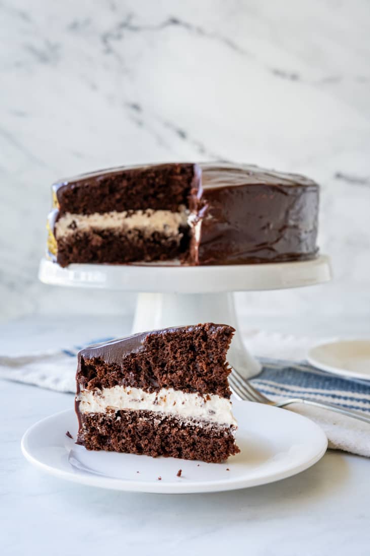 slice of chocolate cake with large cream filling on a plate with cake in the background