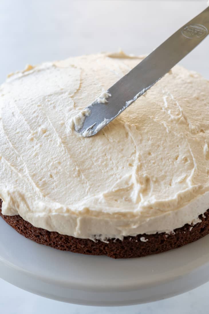 white frosting being spread on chocolate cake