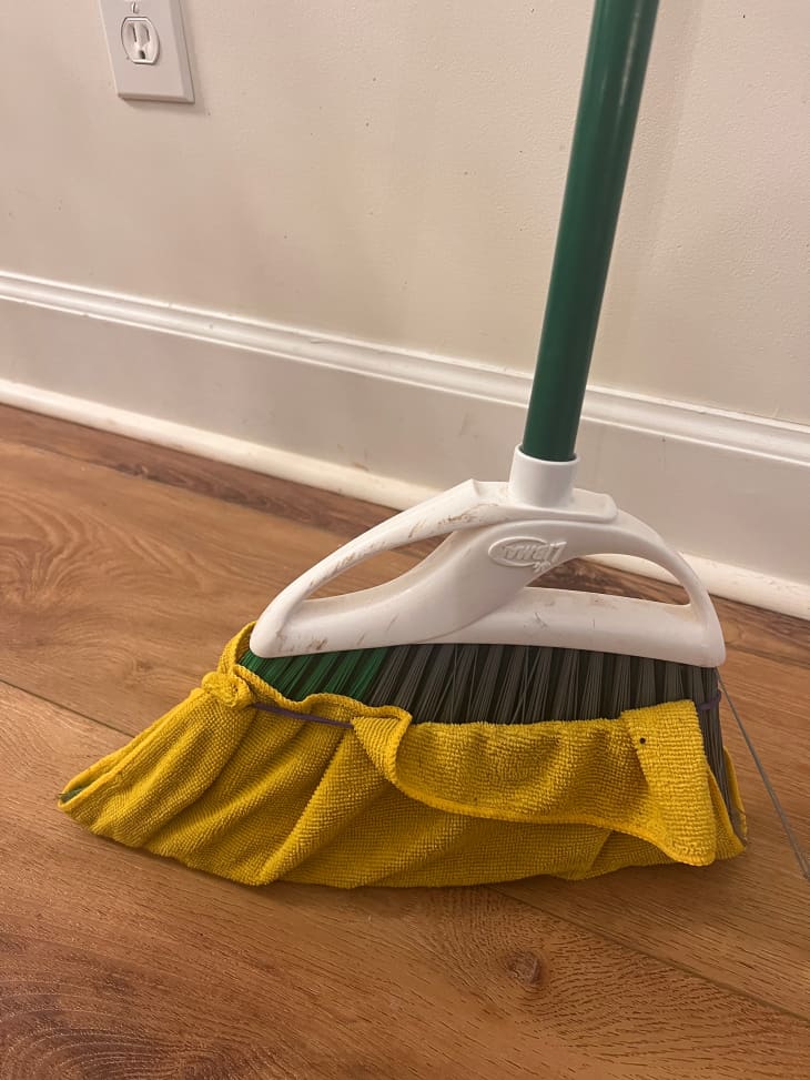 Broom covered with microfiber cloth used for cleaning baseboard.