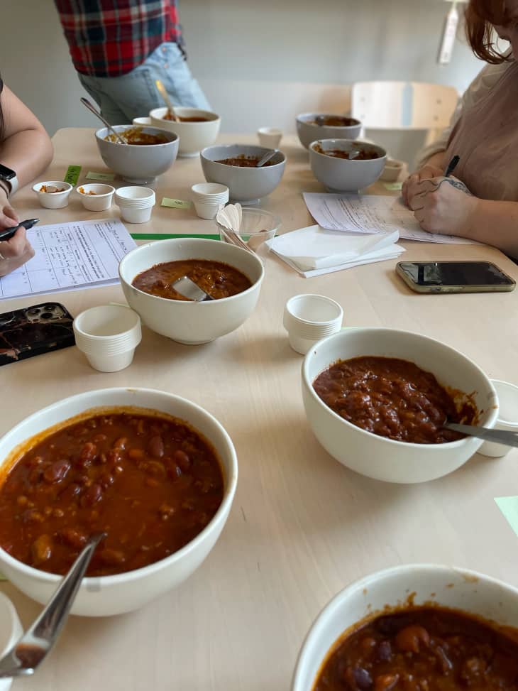 Taste testers rating bowls of canned chili on dining table.