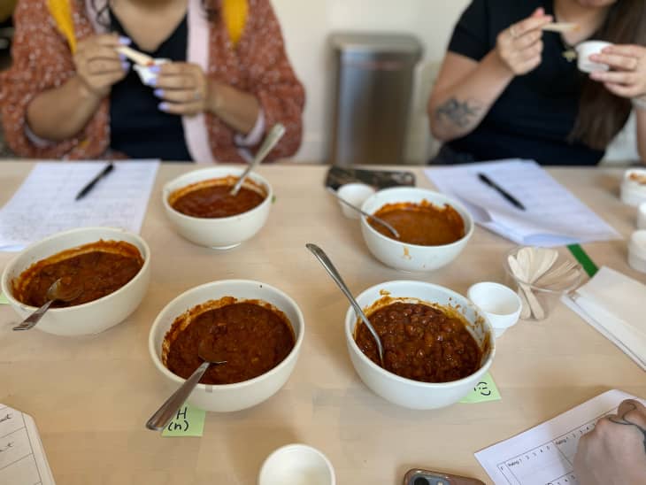 Taste testers rating bowls of canned chili on dining table.