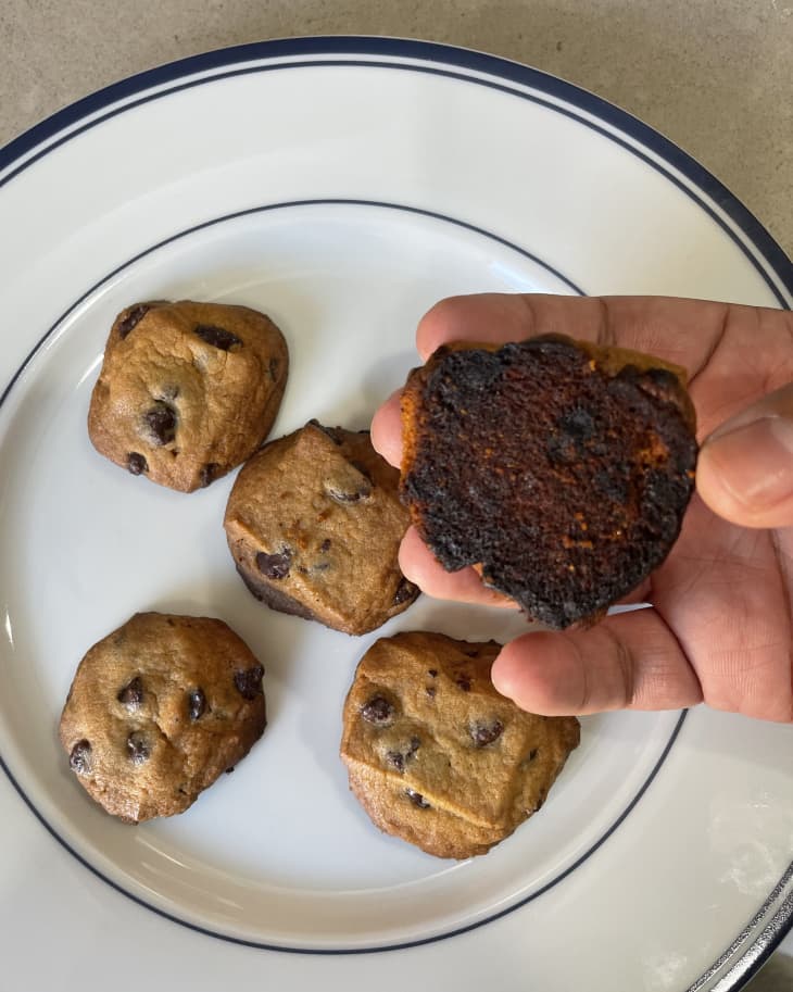 someone holding up a cookie in front of a plate of cookies, showing the burnt bottom