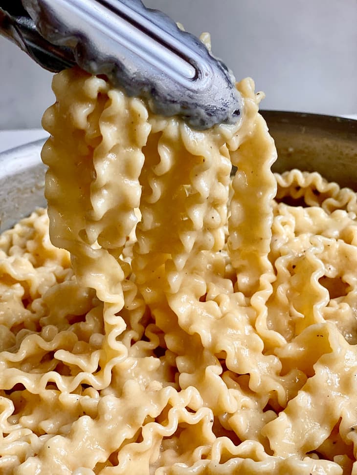 Tongs picking up creamy miso butter pasta in skillet.