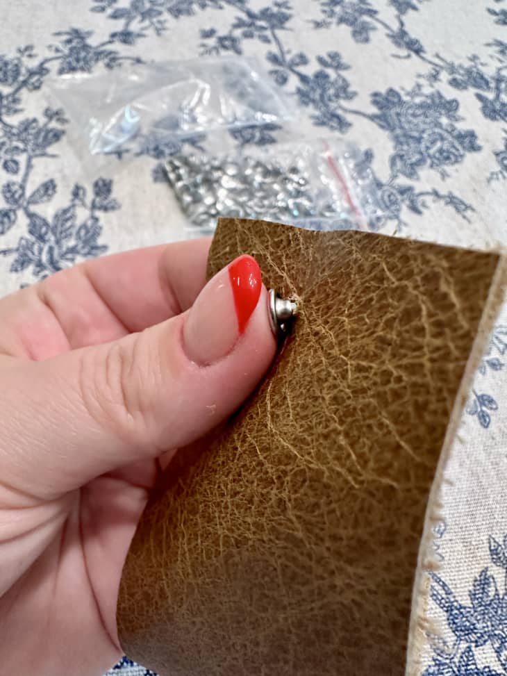 holding a piece of leather and pushing in a grommet