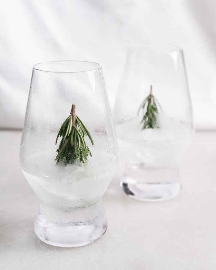 Ice at the bottom of a cocktail glass with a sprig of rosemary sticking out.