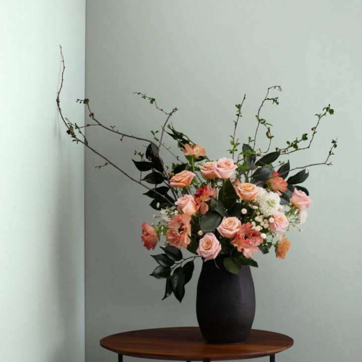 coral floral bouquet on small wood table with light sage walls