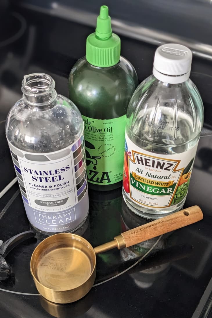 bottles of white vinegar, stainless steel cleaner, and olive oil with gold measuring cup