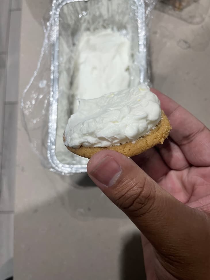 Someone holding chocolate chip cookie topped with cream.