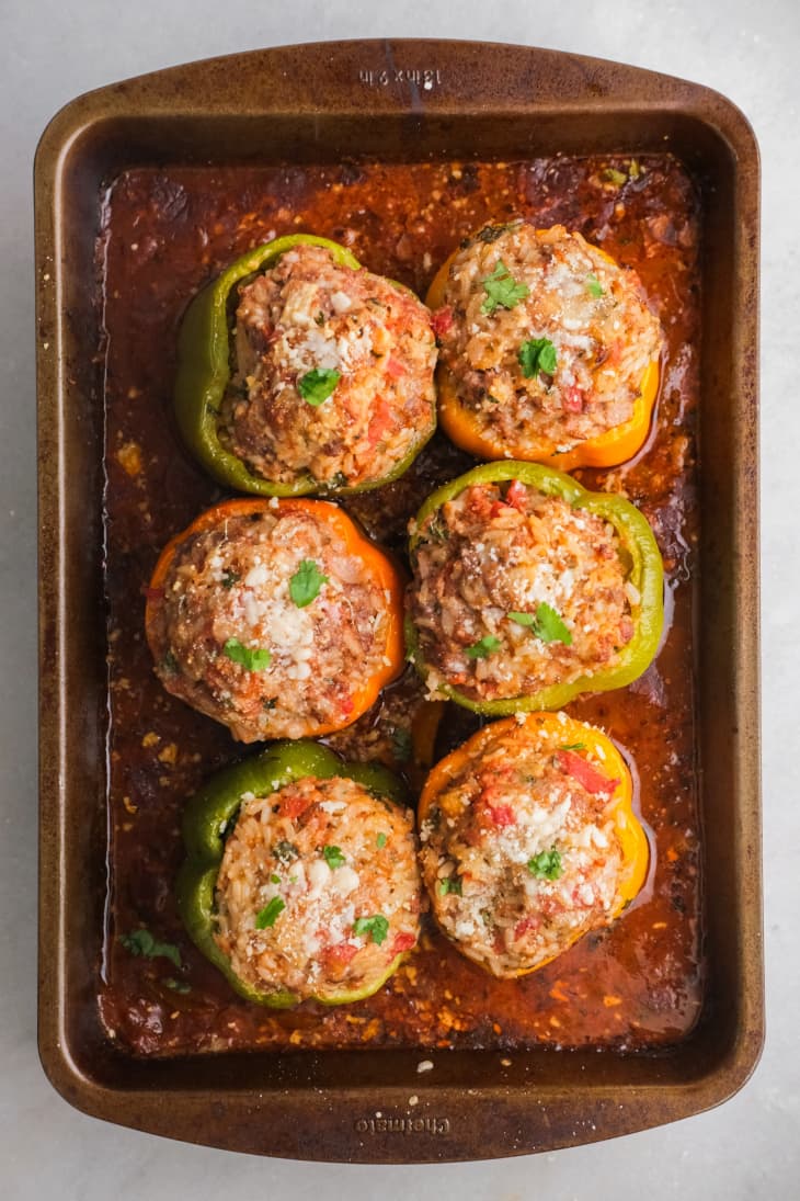 green, orange, and yellow bell peppers stuffed with meat, cheese and herbs on baking sheet