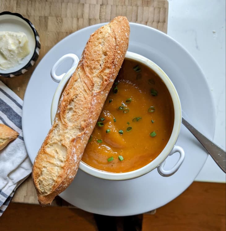 Trader Joe's baguette on the side of a bowl of tomato soup.