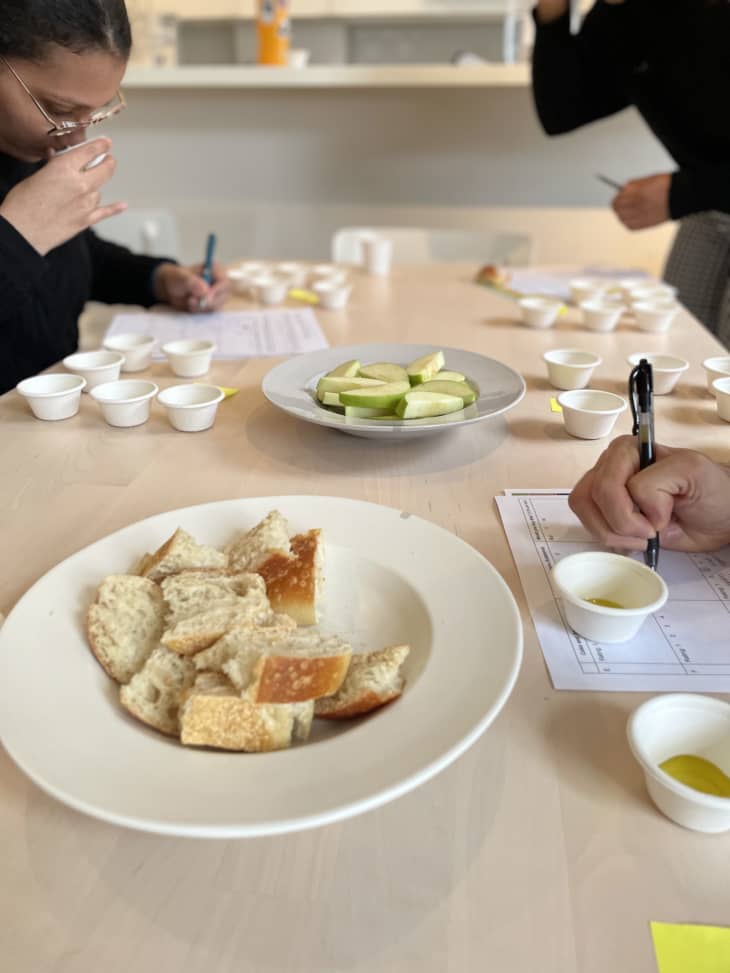Table with test cups of olive oil, people filling out sheets, bowl of bread scraps