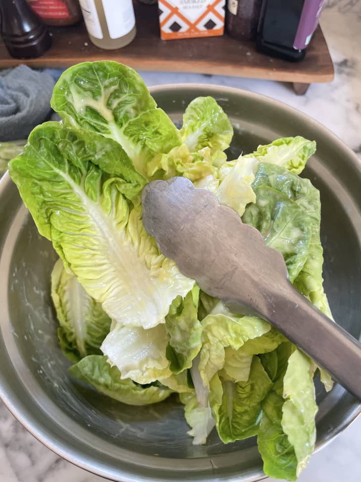 Salad greens getting tossed with vinaigrette with tongs