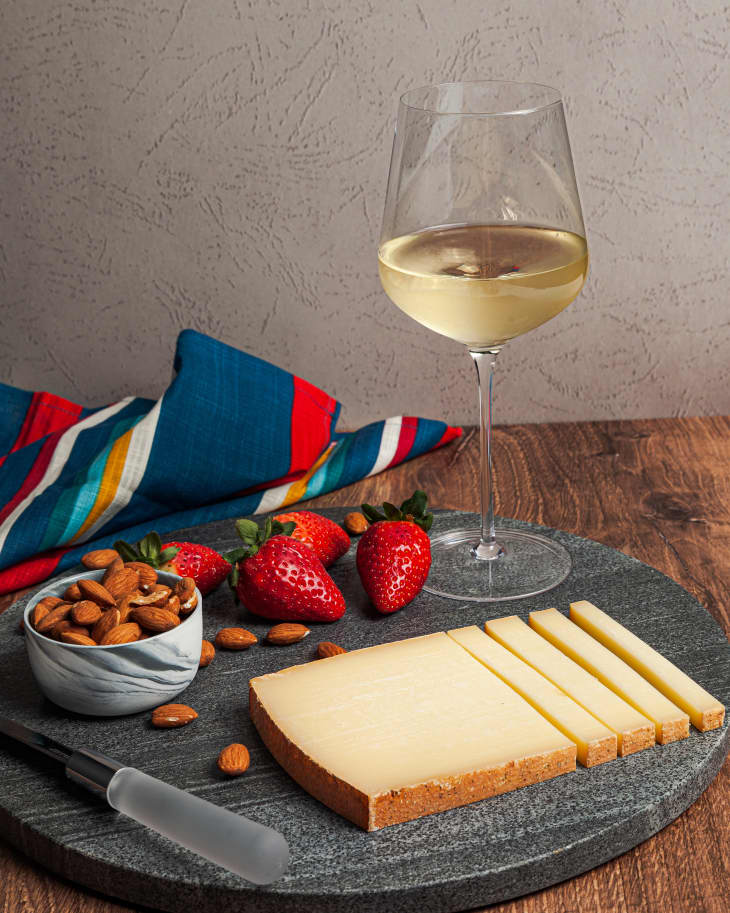 Comtè cheese on a plate with a glass of white wine behind.