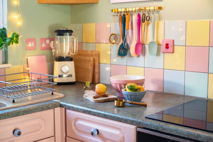 Spoons hang from rod on wall with pastel tiling in kitchen with pastel blender and accessories.