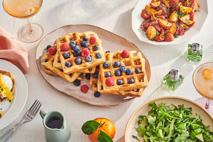 waffles covered with berries on a table with salad, eggs , and potatoes.