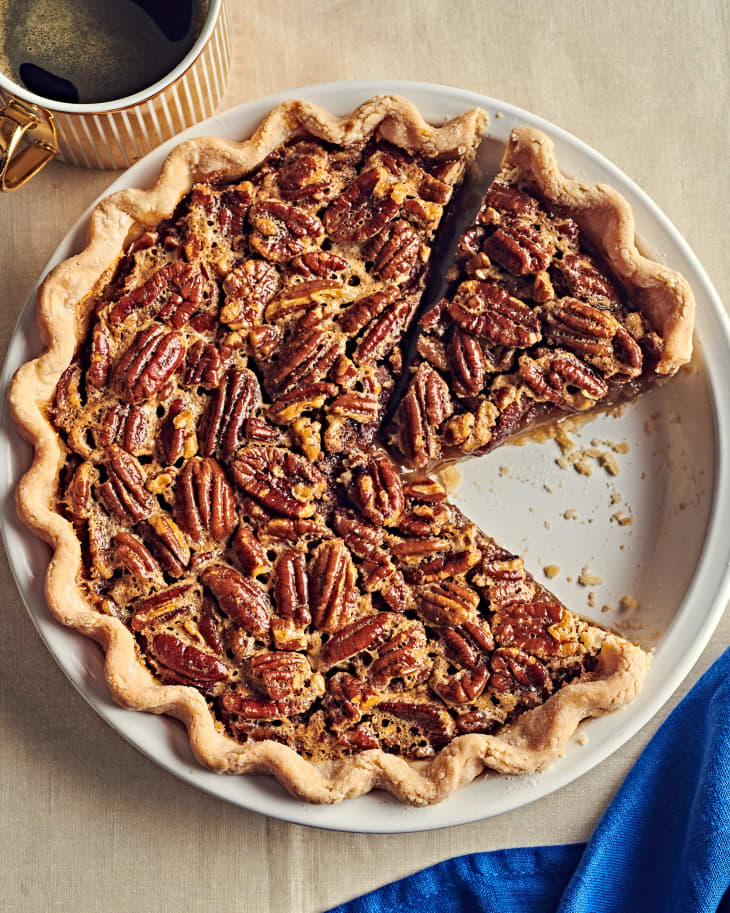 Overhead photo of pecan pie with one slice out on thanksgiving table. Cup of coffee above
