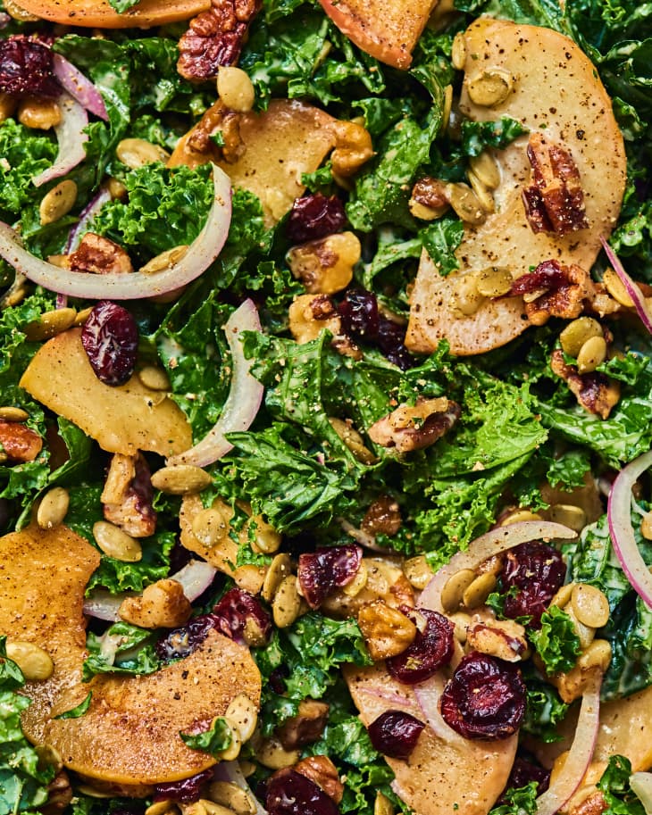overhead close up shot of just-dressed apple kale salad with kale, apple, pecans, red onions