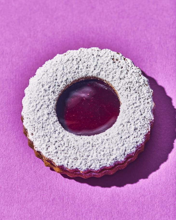 Linzer sandwich cookie with powdered sugar filled with jam on light purple background