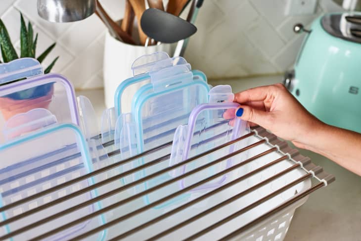 A person placing a container lid into a drying rack with other lids.