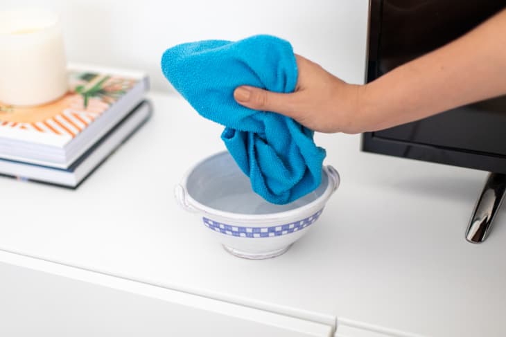 Dipping a cleaning cloth into a small bowl of vinegar