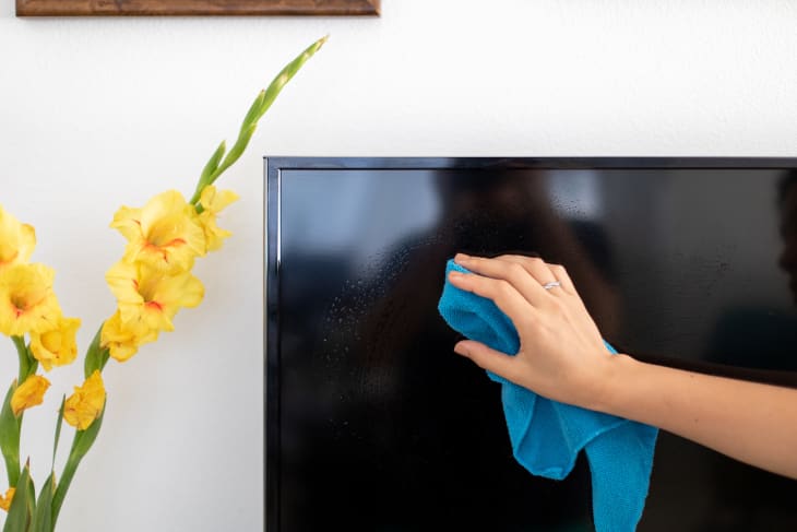 A person wiping down the screen of their television with a microfiber cloth