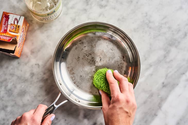 Rubbing a clean pan with box of baking soda and bottle of vinegar nearby