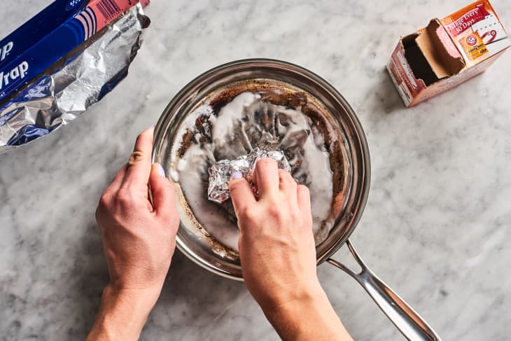 rubbing baking soda paste into a burnt pan with a ball of aluminum foil