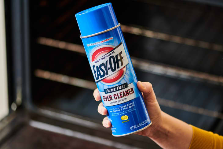 Hand holding a can of Easy-Off Oven Cleaner in front of open oven