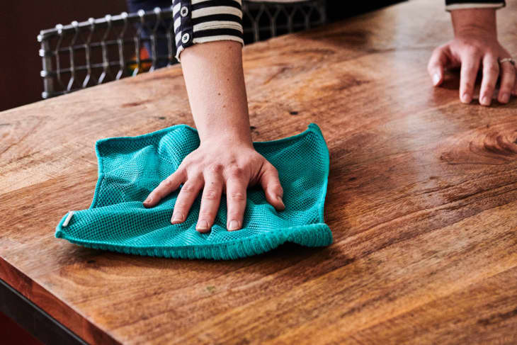 Wiping down a wooden table with a clean, dry microfiber cloth