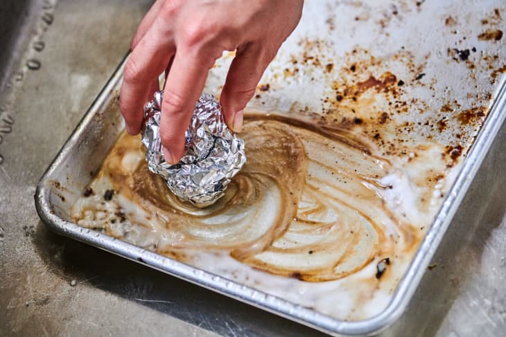 cleaning a dirty baking sheet with a ball of aluminum foil