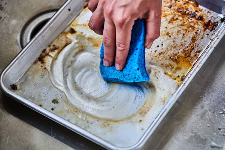 wiping down a dirty baking sheet with a sponge
