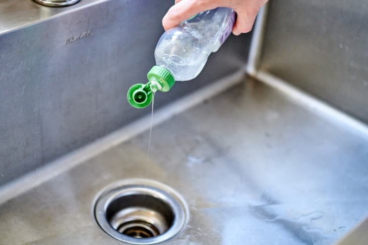 Pouring some dish soap down the drain of a kitchen sink