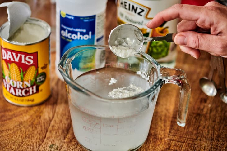 adding some cornstarch to a measuring cup with a mixture of vinegar and rubbing alcohol