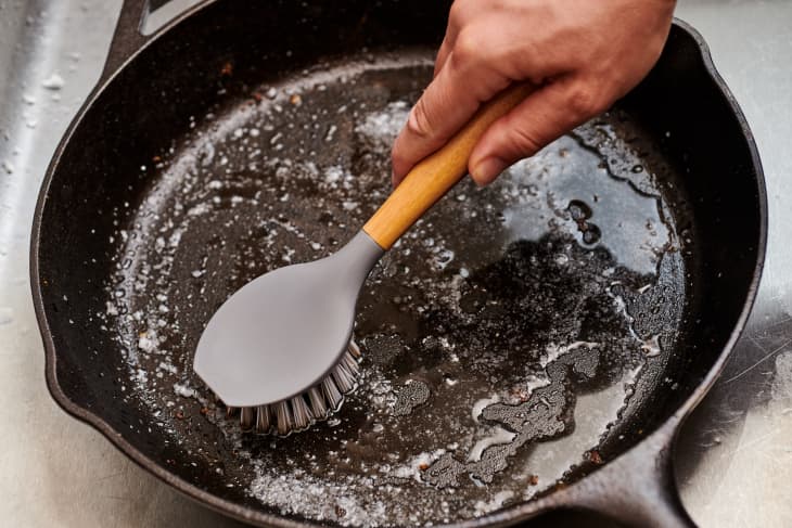 Dirty cast iron skillet being prepared for cleaning with coarse salt, brush,  scraper and dish towel on a counter Stock Photo - Alamy