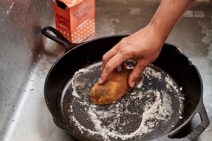 rubbing baking soda into a cast iron skillet with potato half, cut side down