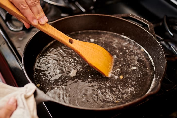 scrapping a cast iron skillet on the stovetop filled with water with a wooden spoon
