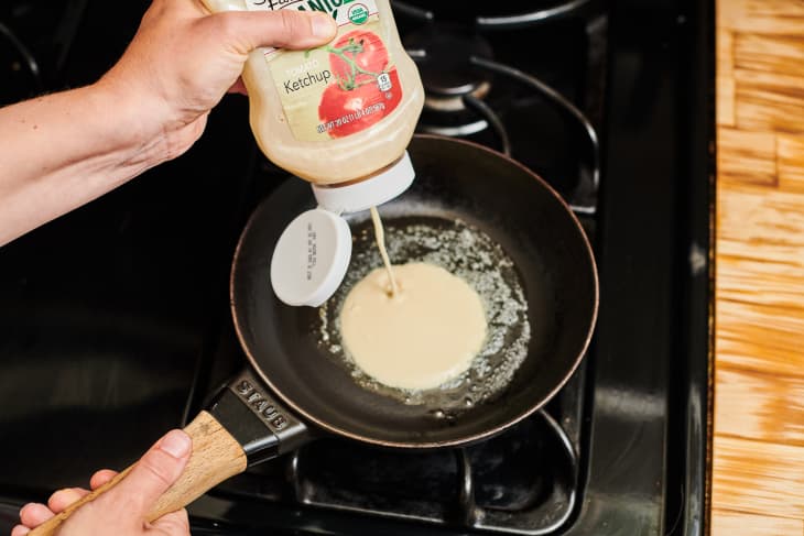 squeezing a bottle of ketchup filled with pancake batter into a skillet