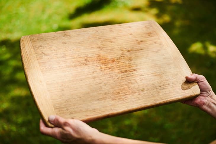 Hands hold cutting board in the sunlight.