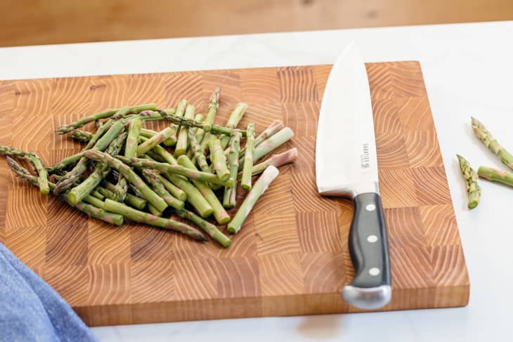 Chopped asparagus on a wooden cutting board with chef's knife out to the side.